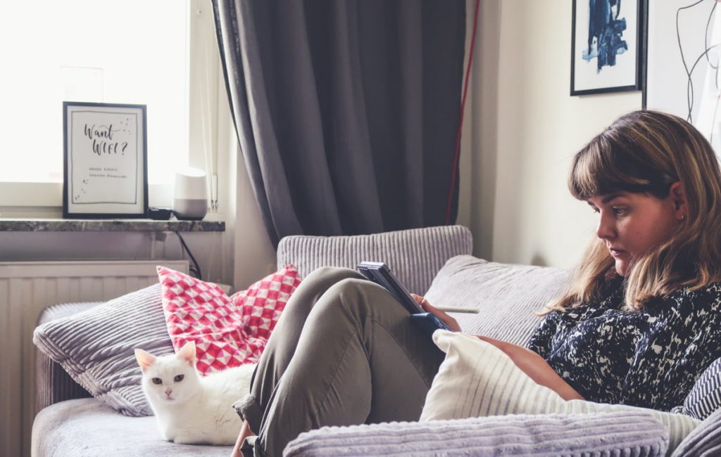 Elin sitter i soffan och läser på en iPad, bredvid ligger hennes vita katt Klara